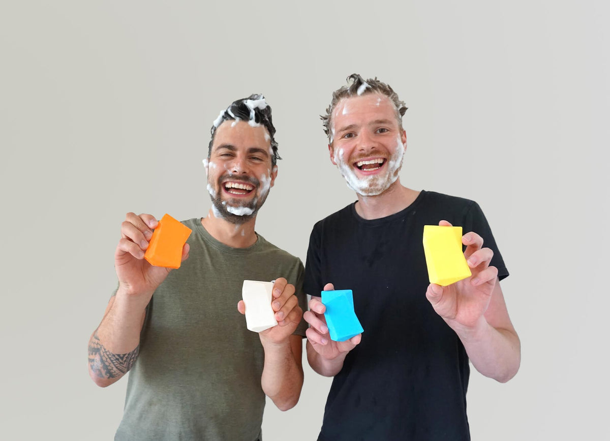 Johannes und Christoph stehen mit Duschbrocken und aufgeschäumten Haaren vor einer Wand