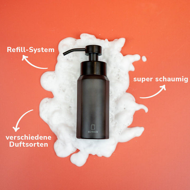 Schwarzer Duschbrocken Seifenspender auf orangem Hintergrund mit weißem Schaum und Hinweisen zu Refill-System und Schaum