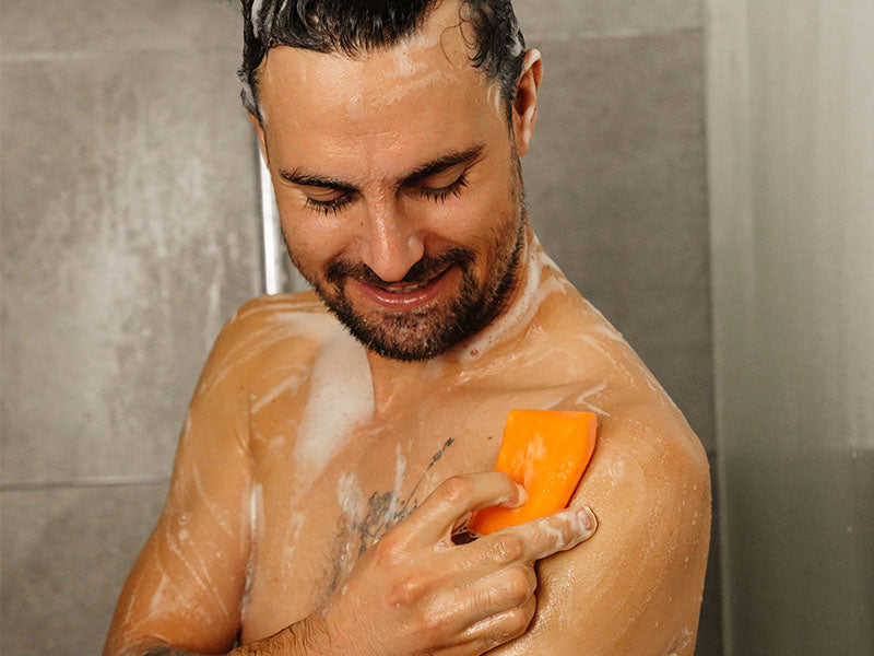 Mann schäumt sich in der Dusche mit Duschbrocken ein