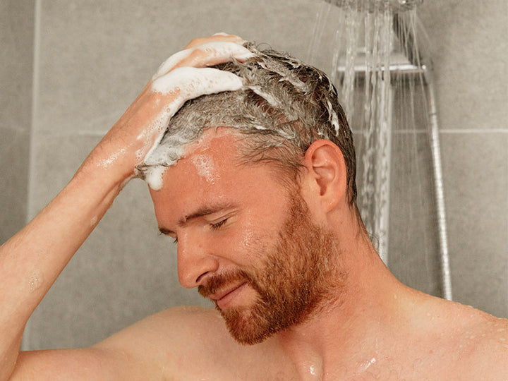 Mann schäumt sich Haar unter der Dusche ein